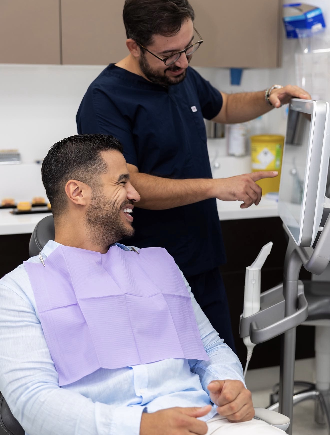 A patient in the dental chair smiling while a clinician explains a scan on screen